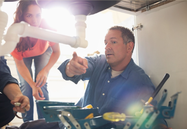 A plumber shows a homeowner completed work under a sink.